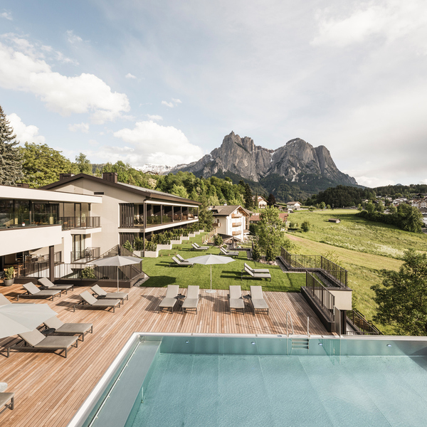 Hotel Alpenflora with sun deck, loungers and outdoor pool overlooking green meadows and the Dolomite peaks of the Schlern in South Tyrol