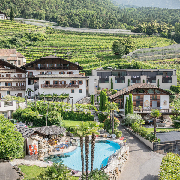 Paloria Apartments & Sport with an outdoor pool, palm trees and traditional buildings, set among vineyards and mountains in South Tyrol